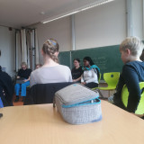 Schüler*innen sitzen im Klassenraum und hören den Trainerinnen zu. 
